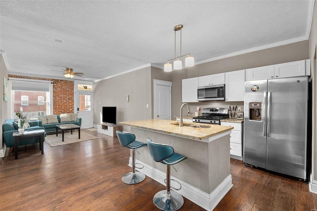 kitchen featuring light stone countertops, white cabinets, stainless steel appliances, an island with sink, and sink