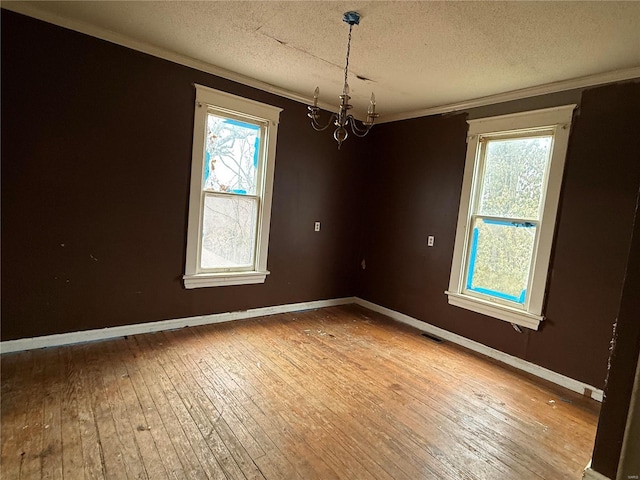 spare room featuring wood-type flooring, plenty of natural light, an inviting chandelier, and a textured ceiling