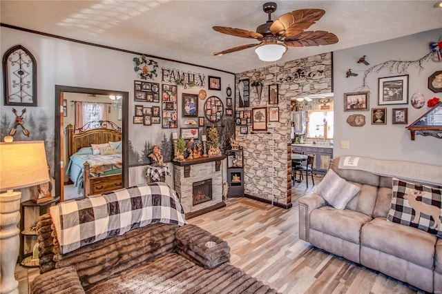 living room featuring ceiling fan, a fireplace, crown molding, light hardwood / wood-style flooring, and a textured ceiling