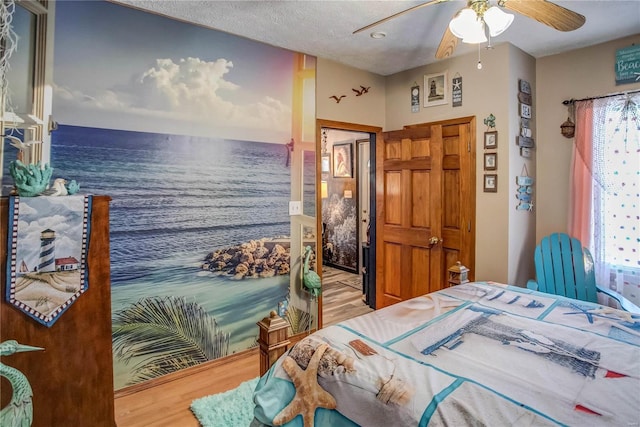 bedroom featuring a textured ceiling, ceiling fan, a water view, and hardwood / wood-style floors