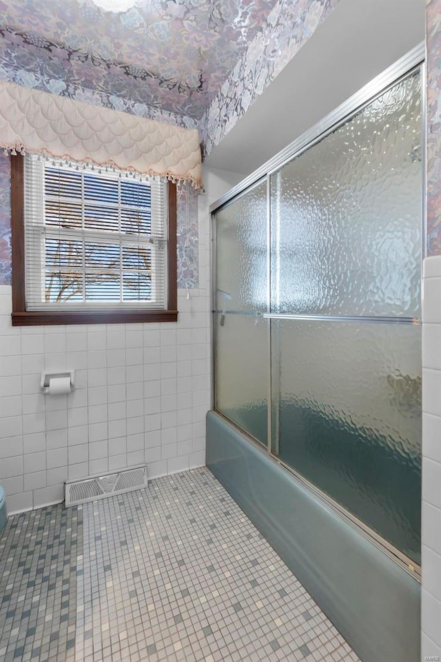 bathroom with combined bath / shower with glass door, tile walls, tile patterned flooring, and toilet