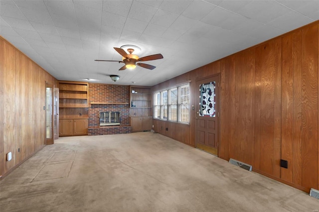 unfurnished living room with ceiling fan, a brick fireplace, wood walls, built in features, and light carpet