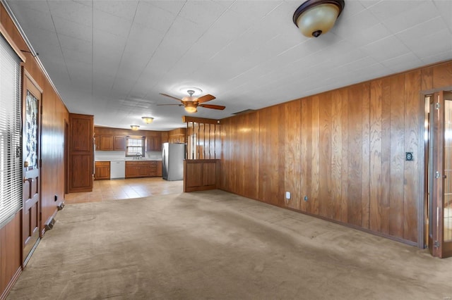 unfurnished living room featuring ceiling fan, light colored carpet, sink, and wood walls