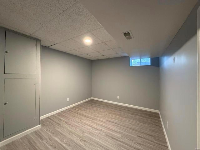 basement featuring a paneled ceiling and light hardwood / wood-style flooring