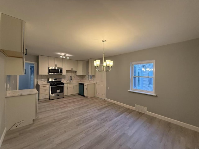 kitchen featuring stainless steel appliances, tasteful backsplash, decorative light fixtures, white cabinets, and light hardwood / wood-style flooring