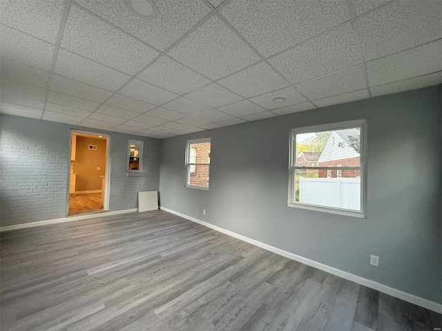 empty room featuring a paneled ceiling, brick wall, and hardwood / wood-style flooring