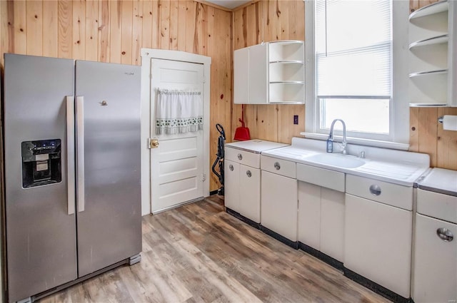 kitchen with wood walls, white cabinetry, sink, stainless steel fridge with ice dispenser, and light wood-type flooring