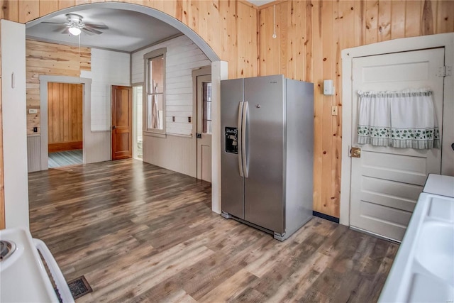 kitchen featuring stainless steel fridge with ice dispenser, wood-type flooring, ceiling fan, and wood walls