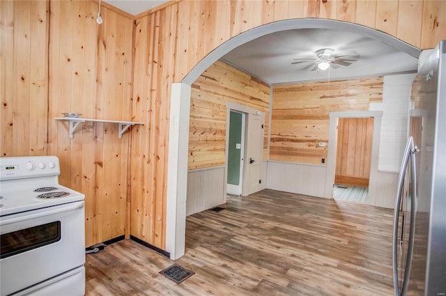 kitchen featuring white electric range oven, wood-type flooring, stainless steel fridge, wooden walls, and ceiling fan