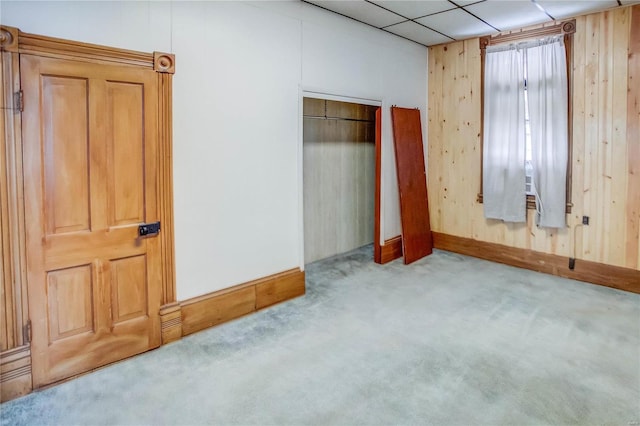 unfurnished bedroom with light colored carpet, wood walls, and a drop ceiling