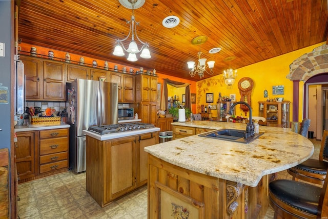 kitchen featuring decorative light fixtures, a notable chandelier, decorative backsplash, sink, and an island with sink