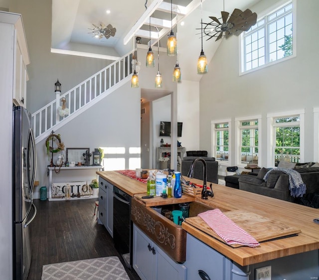 kitchen featuring a towering ceiling, wood counters, hanging light fixtures, stainless steel refrigerator, and ceiling fan