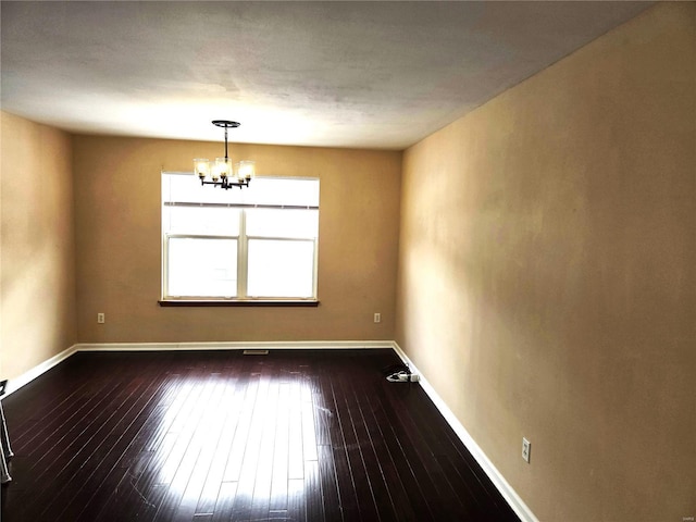 empty room featuring dark hardwood / wood-style flooring and an inviting chandelier