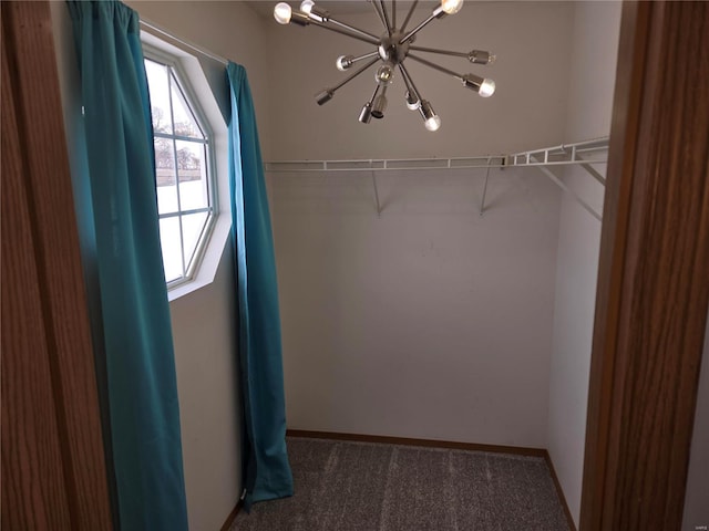 spacious closet featuring dark colored carpet and a chandelier