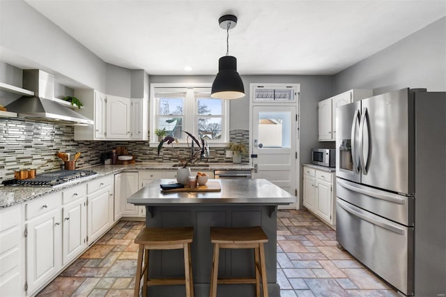 kitchen with white cabinets, appliances with stainless steel finishes, wall chimney range hood, and a kitchen island