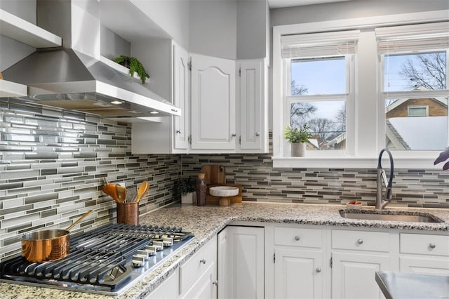 kitchen featuring backsplash, wall chimney range hood, sink, white cabinetry, and stainless steel gas cooktop