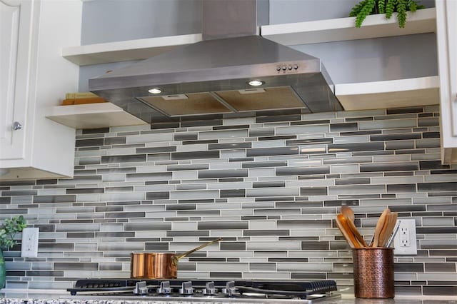 interior details with tasteful backsplash, white cabinets, and island exhaust hood