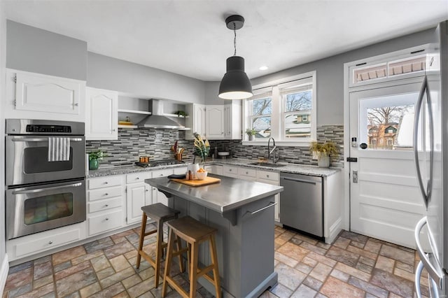 kitchen with appliances with stainless steel finishes, wall chimney exhaust hood, white cabinets, and a center island