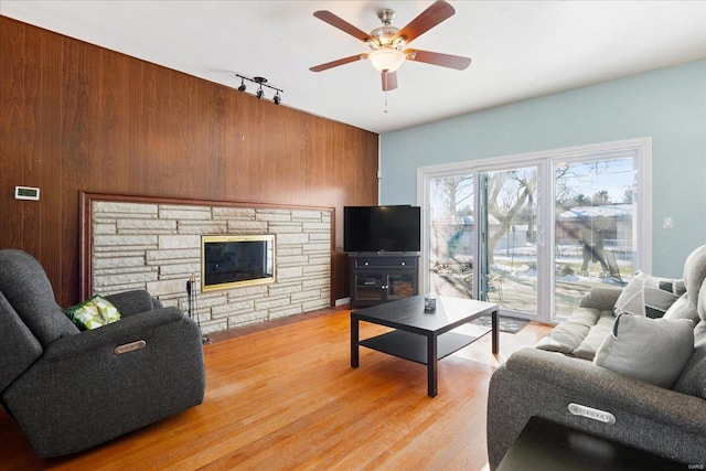 living room featuring ceiling fan, a fireplace, wood walls, and light hardwood / wood-style flooring