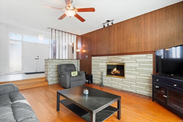 living room with ceiling fan, light wood-type flooring, a fireplace, and wood walls