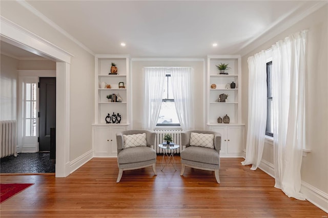 living area with wood-type flooring, built in shelves, and radiator heating unit