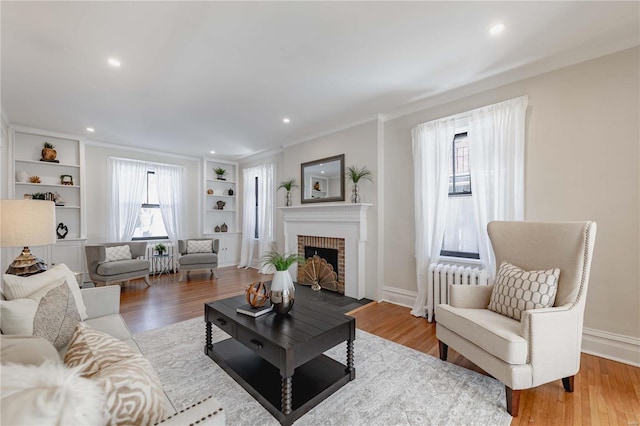 living room with a brick fireplace, a wealth of natural light, light hardwood / wood-style flooring, and ornamental molding