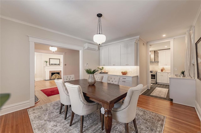 dining room featuring an AC wall unit, a fireplace, crown molding, and hardwood / wood-style flooring