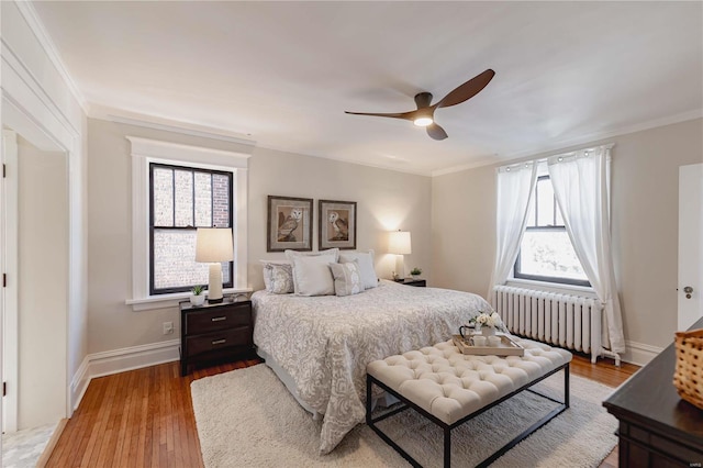 bedroom featuring ceiling fan, radiator heating unit, multiple windows, and hardwood / wood-style flooring