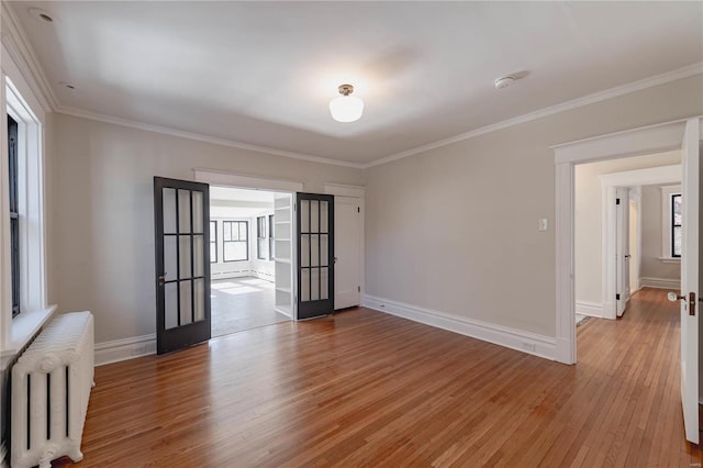 empty room with radiator heating unit, crown molding, french doors, and light hardwood / wood-style flooring