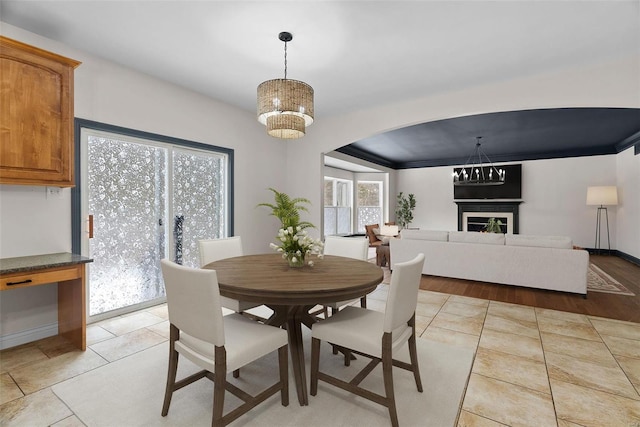 dining area with baseboards, arched walkways, a warm lit fireplace, and light tile patterned flooring