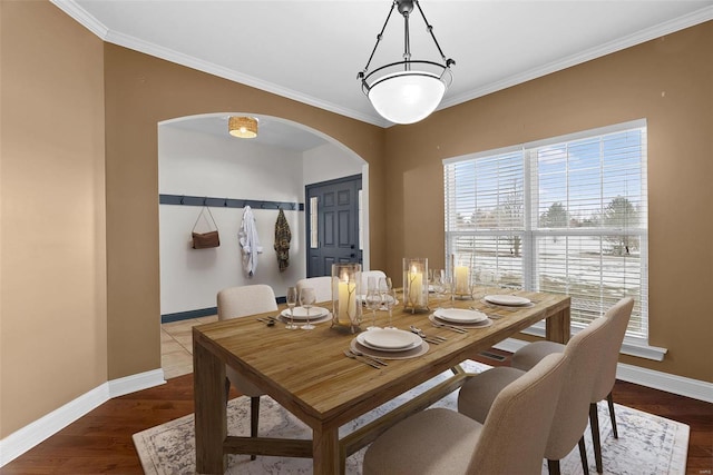 dining space featuring arched walkways, crown molding, baseboards, and wood finished floors