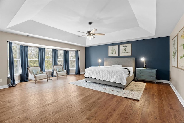 bedroom with ceiling fan, wood-type flooring, and a tray ceiling