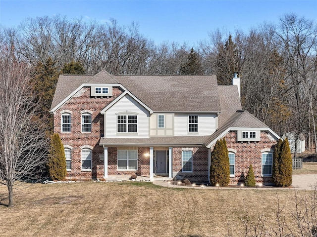 view of front of property featuring a shingled roof, a front yard, brick siding, and a chimney