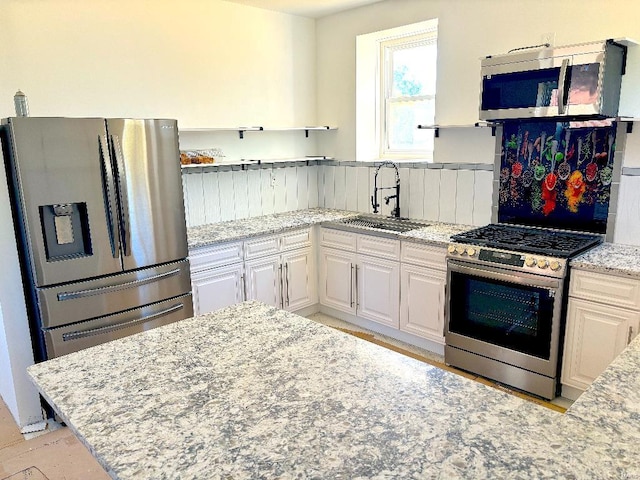 kitchen featuring white cabinetry, stainless steel appliances, sink, and light stone counters