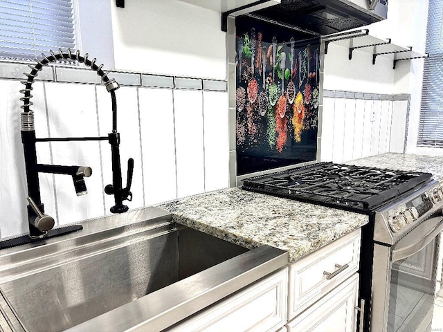 kitchen featuring gas range, light stone countertops, and white cabinets