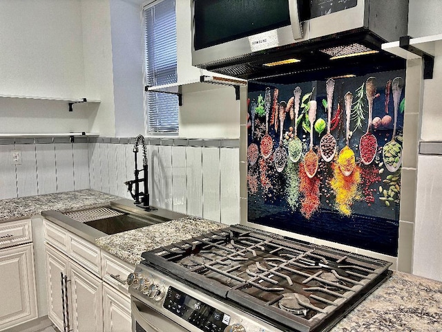 kitchen with sink, appliances with stainless steel finishes, tasteful backsplash, light stone counters, and white cabinets