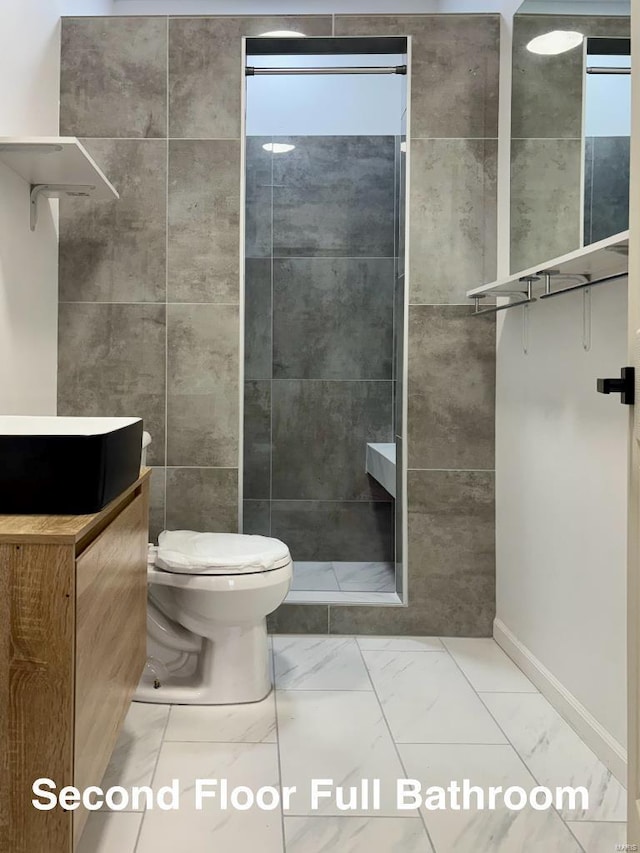 bathroom with vanity, tiled shower, tile walls, and toilet