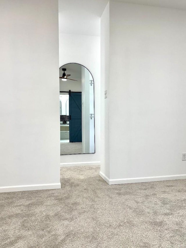 spare room with ceiling fan, a barn door, and carpet