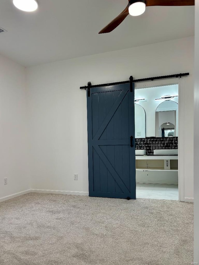 empty room featuring ceiling fan, a barn door, and light carpet