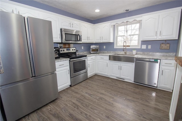 kitchen featuring appliances with stainless steel finishes, decorative light fixtures, sink, white cabinets, and dark hardwood / wood-style flooring