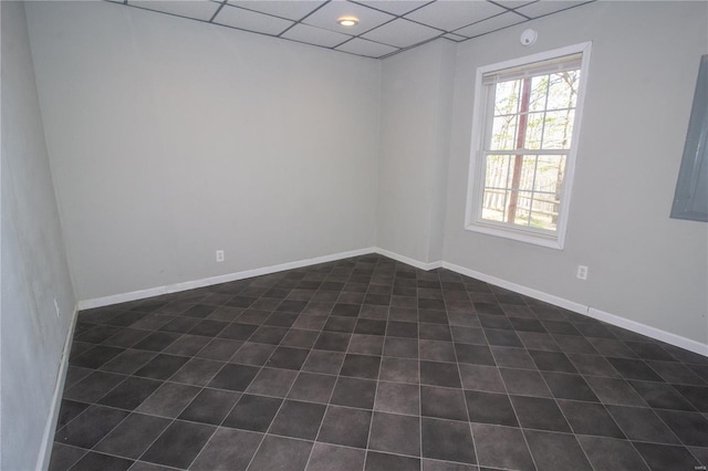 spare room with a paneled ceiling, dark tile patterned floors, and baseboards