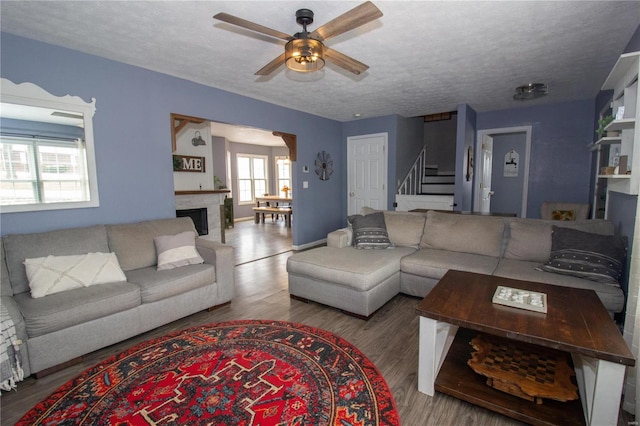 living room featuring a ceiling fan, a textured ceiling, a fireplace, stairway, and wood finished floors