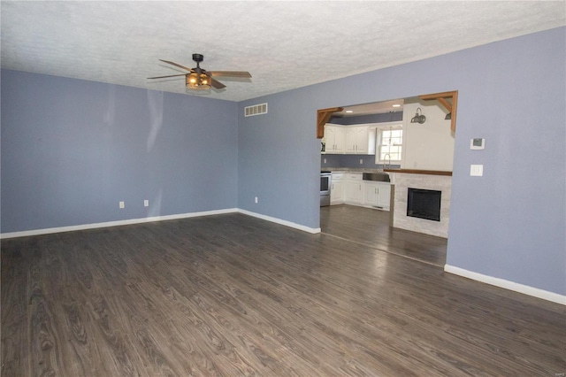 unfurnished living room with dark wood-style flooring, baseboards, a ceiling fan, and a textured ceiling