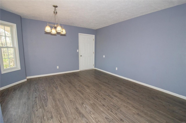 empty room featuring a chandelier, a textured ceiling, baseboards, and dark wood-style floors
