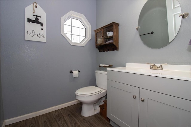 half bath with toilet, vanity, wood finished floors, and baseboards