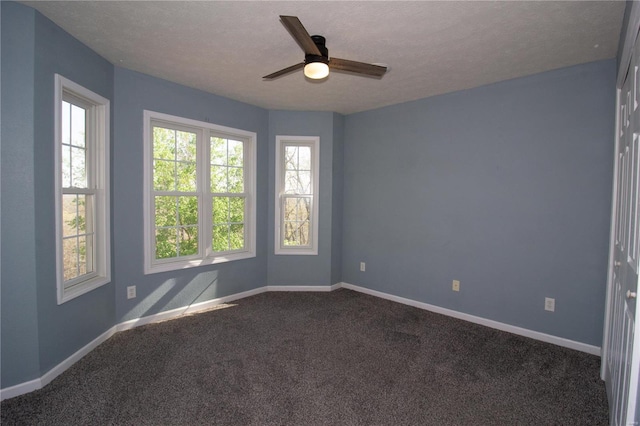 empty room featuring dark carpet, a textured ceiling, baseboards, and a ceiling fan