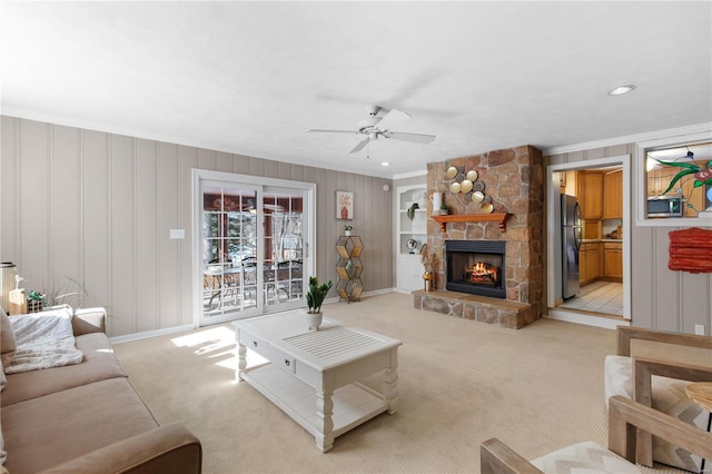 living room featuring light carpet, a stone fireplace, crown molding, and ceiling fan