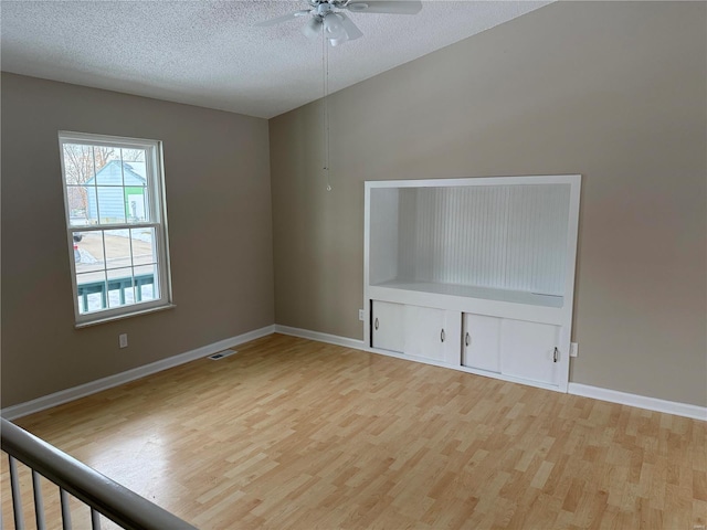 empty room with a textured ceiling, ceiling fan, and light hardwood / wood-style flooring