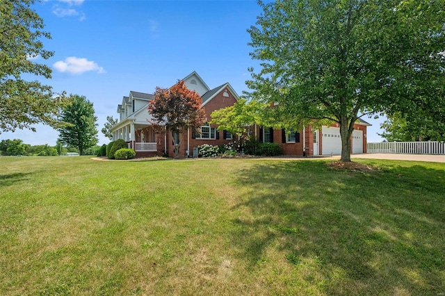 view of property hidden behind natural elements featuring a garage, a front lawn, and covered porch