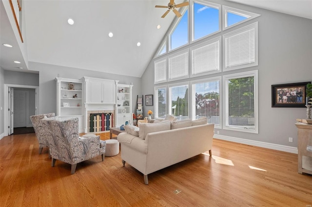 living room featuring ceiling fan, built in shelves, light hardwood / wood-style flooring, and high vaulted ceiling